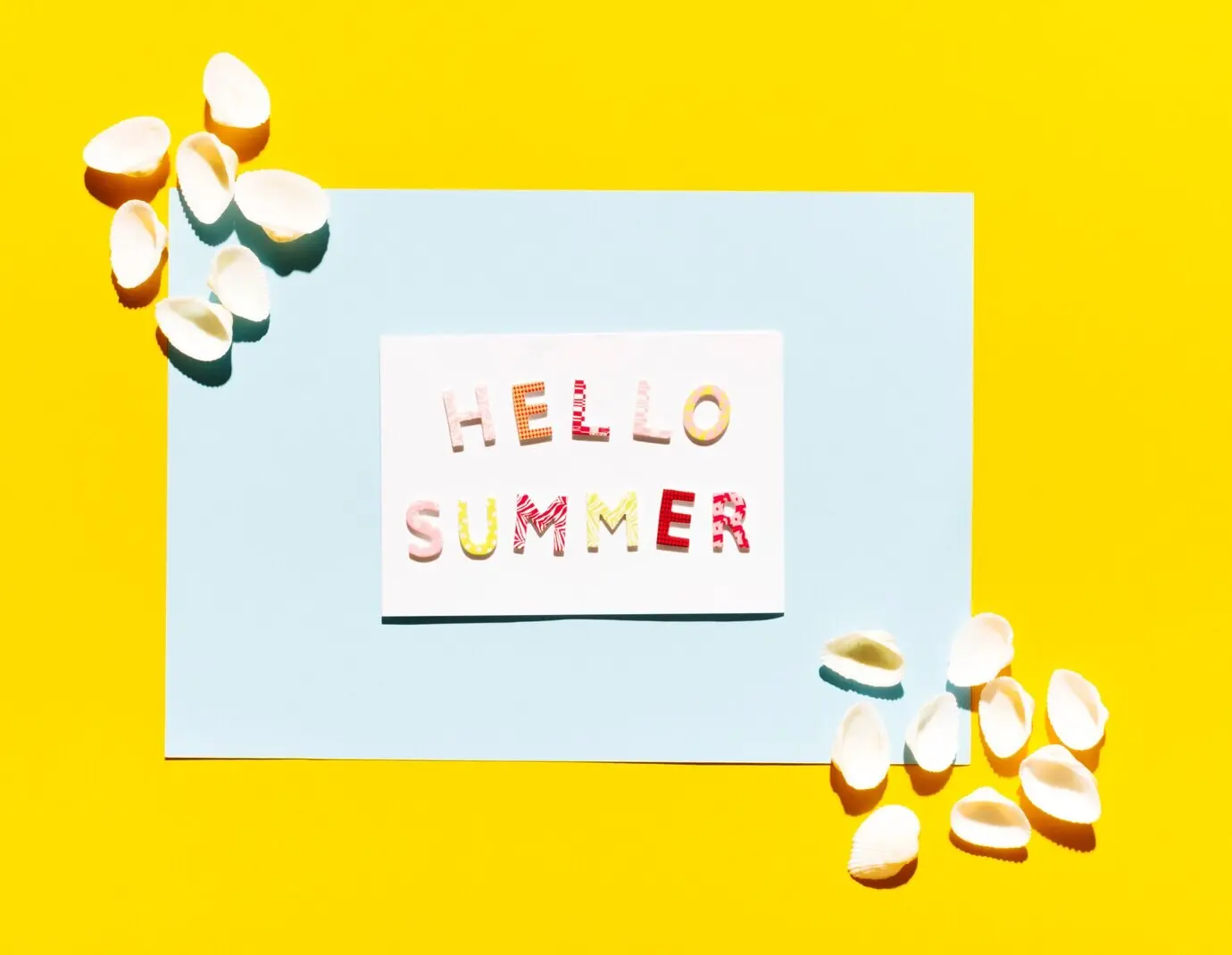 Papier mit dem Schriftzug „Hello Summer“ und Muscheln.